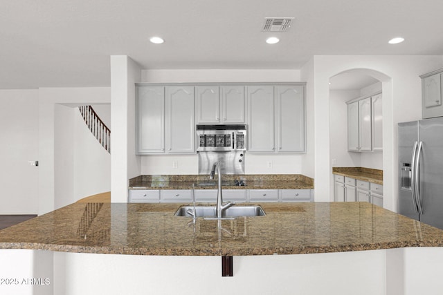 kitchen with visible vents, an island with sink, dark stone countertops, stainless steel appliances, and a sink