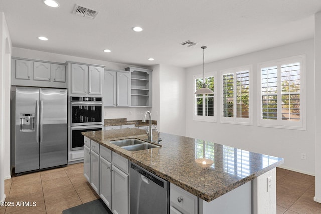 kitchen with a center island with sink, hanging light fixtures, stainless steel appliances, open shelves, and a sink