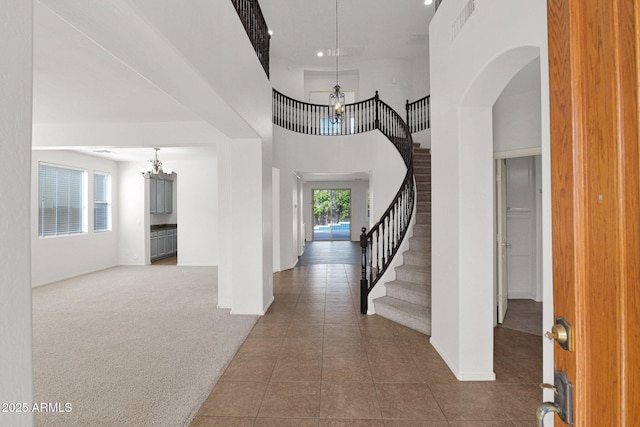 entrance foyer with stairs, carpet floors, a towering ceiling, and tile patterned floors