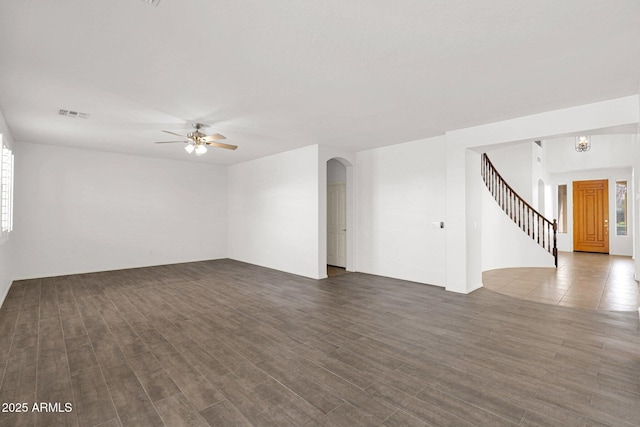 spare room featuring arched walkways, ceiling fan with notable chandelier, visible vents, stairs, and dark wood finished floors