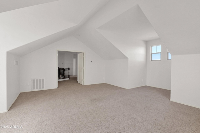 additional living space with lofted ceiling, visible vents, and light colored carpet