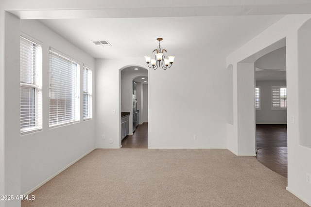 empty room featuring plenty of natural light, dark colored carpet, visible vents, and a notable chandelier