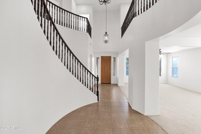 foyer entrance with a ceiling fan, baseboards, stairway, tile patterned floors, and carpet