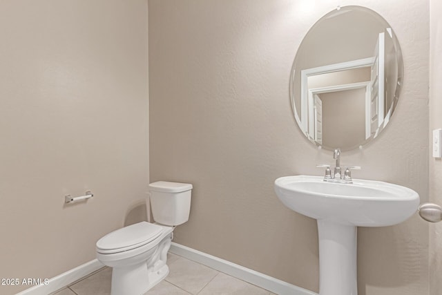 half bath featuring baseboards, tile patterned floors, and toilet