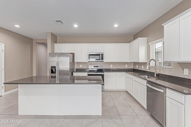 kitchen featuring visible vents, a kitchen island, dark countertops, a sink, and stainless steel appliances