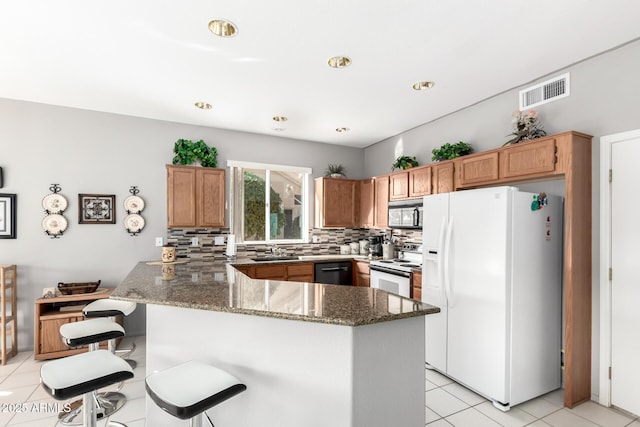 kitchen with kitchen peninsula, a kitchen bar, white appliances, sink, and dark stone countertops