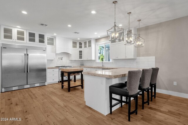 kitchen featuring light hardwood / wood-style floors, a notable chandelier, white cabinetry, kitchen peninsula, and premium appliances