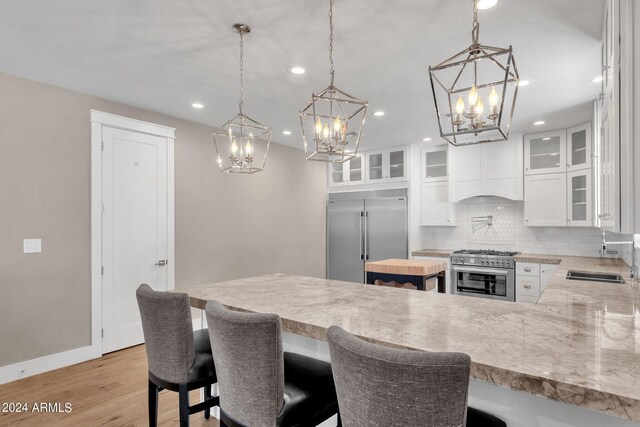 kitchen with sink, a notable chandelier, white cabinetry, kitchen peninsula, and premium appliances