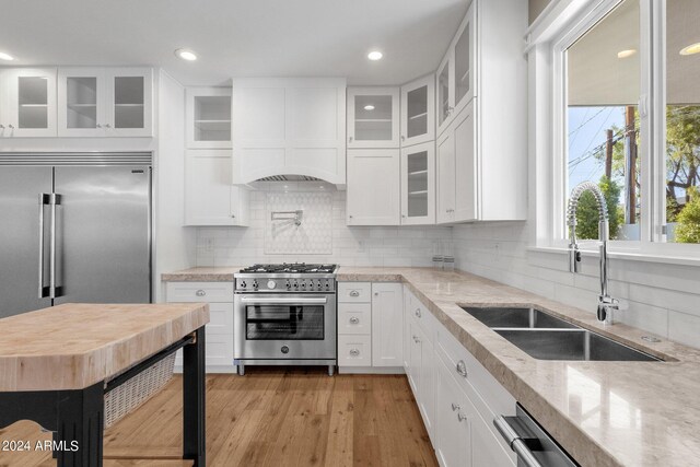 kitchen featuring high end stainless steel range oven, white cabinetry, sink, and custom exhaust hood