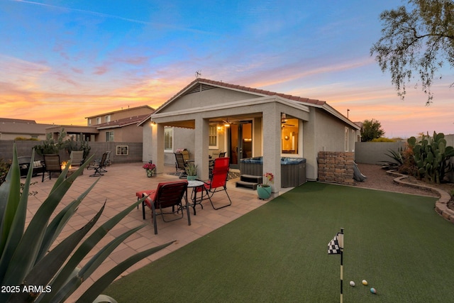 back of property at dusk with a tile roof, stucco siding, a hot tub, a patio area, and a fenced backyard