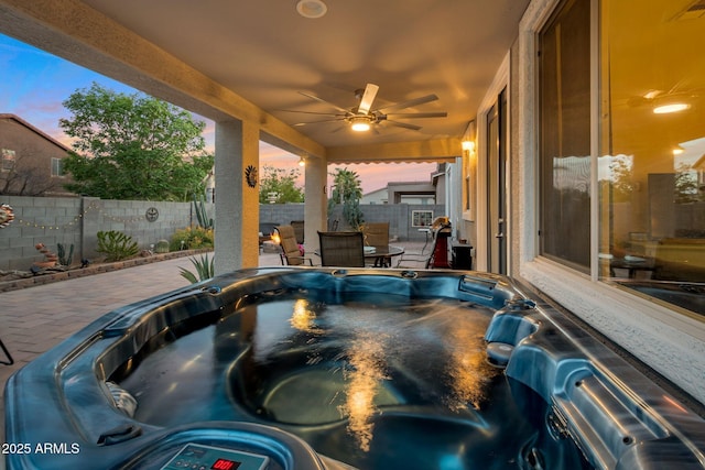 patio terrace at dusk featuring a hot tub, fence, visible vents, and a ceiling fan