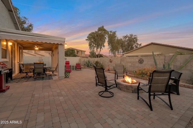 patio terrace at dusk featuring outdoor dining space, a fenced backyard, a fire pit, and a gazebo