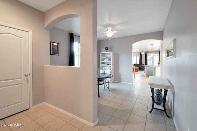 hallway featuring arched walkways, light tile patterned floors, and baseboards