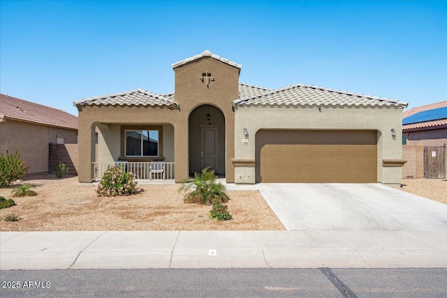 mediterranean / spanish house with stucco siding, a tile roof, covered porch, concrete driveway, and an attached garage