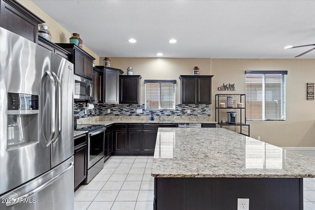 kitchen with light stone counters, light tile patterned flooring, decorative backsplash, appliances with stainless steel finishes, and a center island