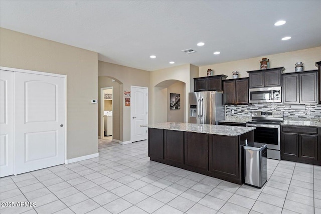 kitchen featuring visible vents, backsplash, a kitchen island, light stone counters, and stainless steel appliances