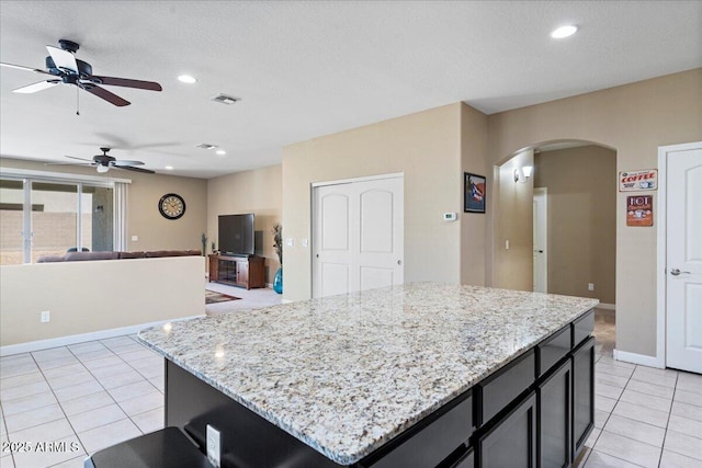 kitchen featuring dark cabinetry, light stone counters, light tile patterned floors, recessed lighting, and arched walkways