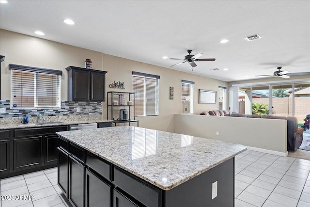 kitchen featuring a sink, tasteful backsplash, open floor plan, a center island, and light tile patterned flooring