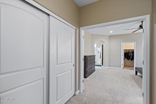 hall with arched walkways, light colored carpet, and baseboards