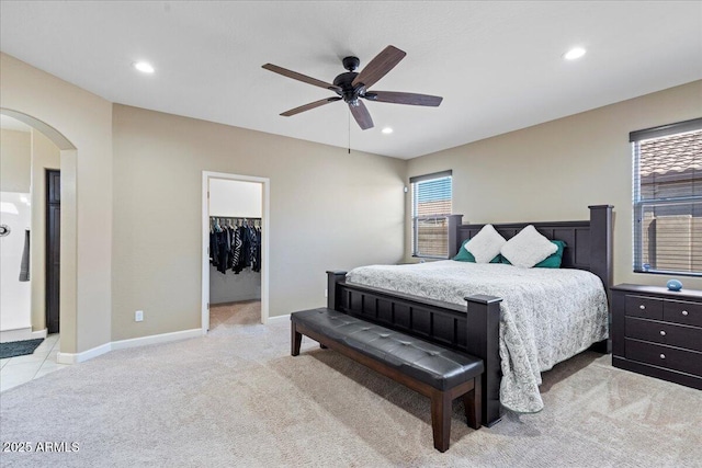 carpeted bedroom with arched walkways, recessed lighting, a walk in closet, and baseboards