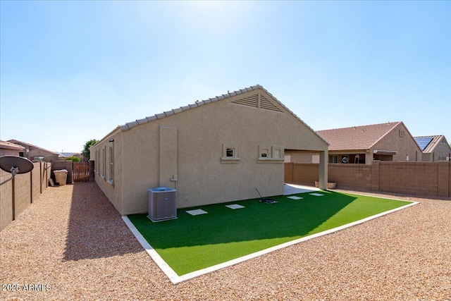 rear view of house featuring a fenced backyard, a lawn, central AC, and stucco siding