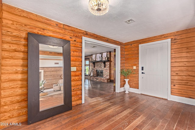 entryway with hardwood / wood-style flooring, an inviting chandelier, a textured ceiling, and a brick fireplace