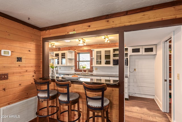 kitchen featuring sink, light wood-type flooring, wooden walls, and a breakfast bar area