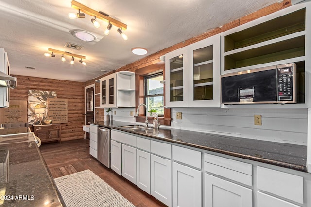 kitchen with wood walls, sink, stainless steel dishwasher, dark hardwood / wood-style flooring, and white cabinetry