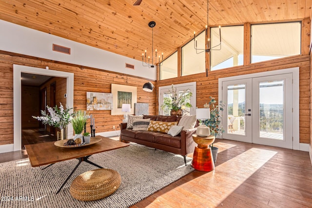 living room featuring hardwood / wood-style floors, wood walls, high vaulted ceiling, french doors, and a notable chandelier