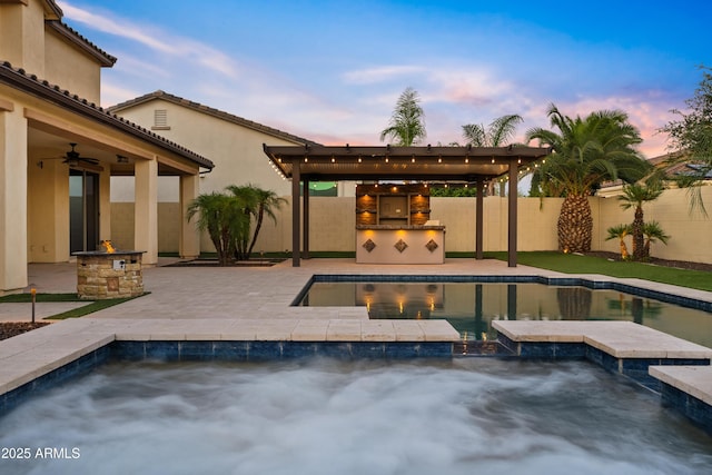 10331 E Starion Ave, Mesa, AZ 85212 - pool at dusk with an in-ground hot tub, exterior kitchen, a fenced backyard, a ceiling fan, and a patio