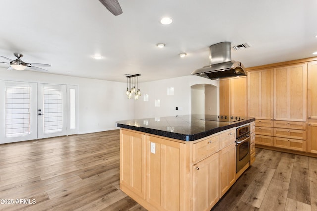 kitchen featuring a center island, island exhaust hood, light brown cabinetry, decorative light fixtures, and stainless steel oven