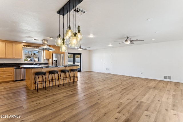 kitchen with appliances with stainless steel finishes, a breakfast bar, decorative light fixtures, light brown cabinets, and light hardwood / wood-style flooring