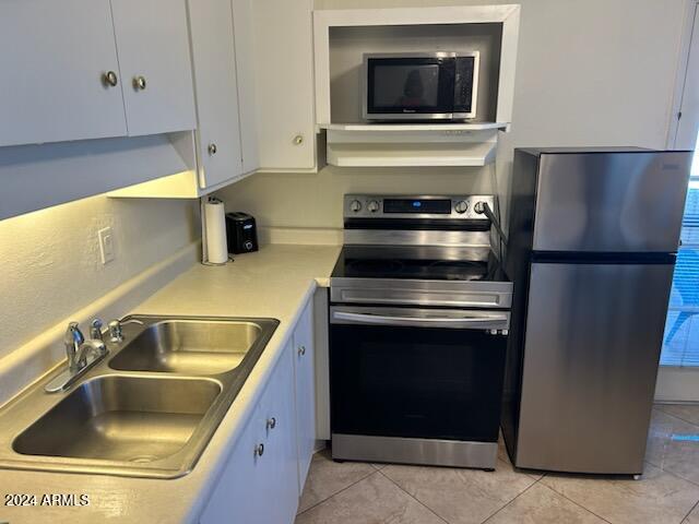 kitchen featuring light tile patterned flooring, appliances with stainless steel finishes, white cabinetry, and sink