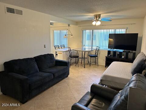 living room featuring ceiling fan, light tile patterned flooring, and a textured ceiling