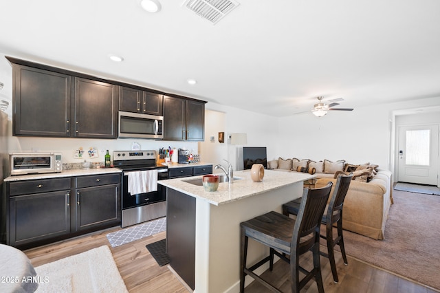 kitchen with sink, a breakfast bar area, stainless steel appliances, a center island with sink, and light hardwood / wood-style flooring