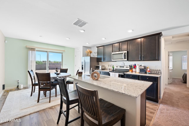 kitchen featuring sink, stainless steel appliances, light stone counters, an island with sink, and a kitchen bar