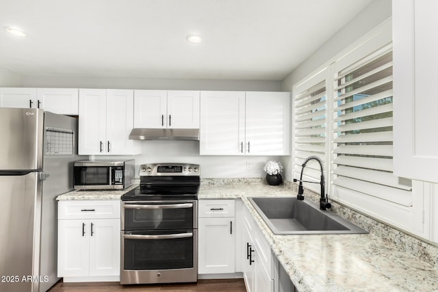 kitchen with a sink, white cabinetry, light stone countertops, under cabinet range hood, and stainless steel appliances
