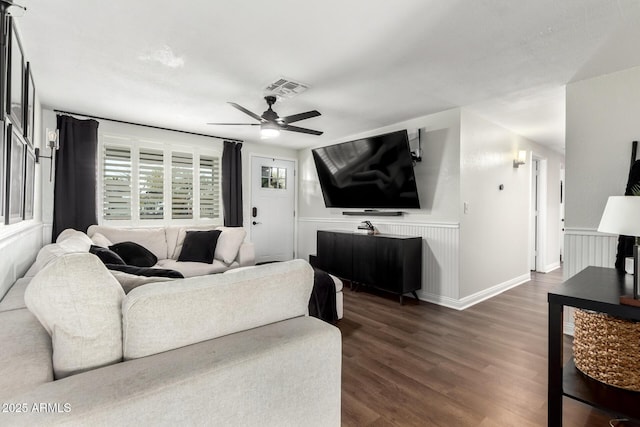 living room featuring dark wood-style flooring, a wainscoted wall, visible vents, and ceiling fan
