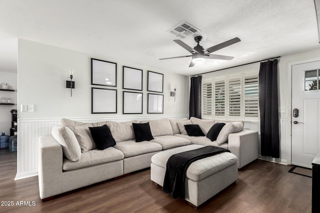 living room with a textured ceiling, visible vents, a ceiling fan, and dark wood-style flooring