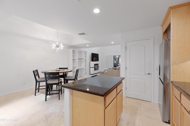 kitchen with stainless steel refrigerator, light brown cabinetry, a chandelier, a center island, and light tile patterned floors