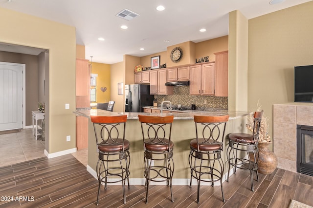 kitchen with a breakfast bar area, a tiled fireplace, kitchen peninsula, and stainless steel refrigerator with ice dispenser