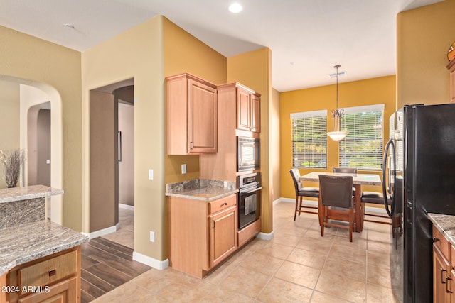 kitchen with wall oven, light stone counters, built in microwave, black refrigerator, and light tile floors