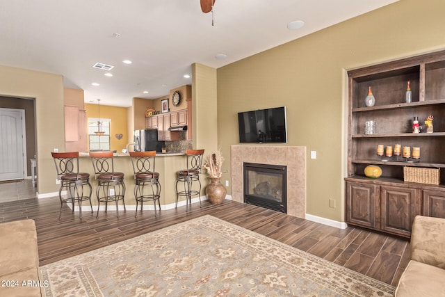 living room featuring ceiling fan, a tile fireplace, and dark wood-type flooring