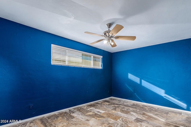 unfurnished room with stone finish flooring, baseboards, and ceiling fan