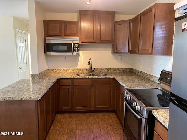 kitchen featuring dark wood-type flooring, sink, appliances with stainless steel finishes, light stone counters, and kitchen peninsula