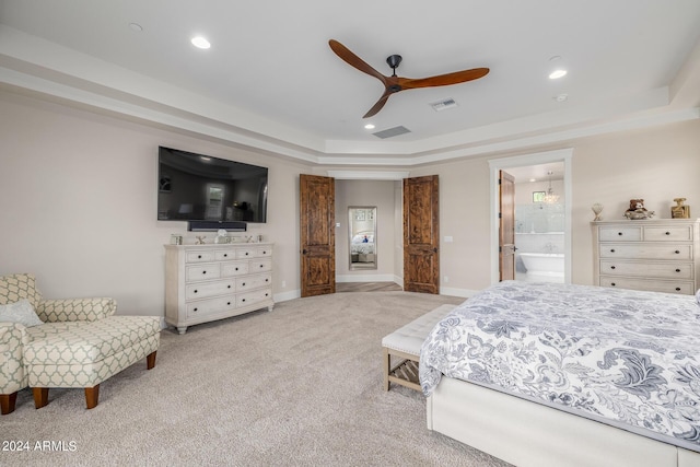 bedroom with ceiling fan, light colored carpet, ensuite bathroom, and a tray ceiling