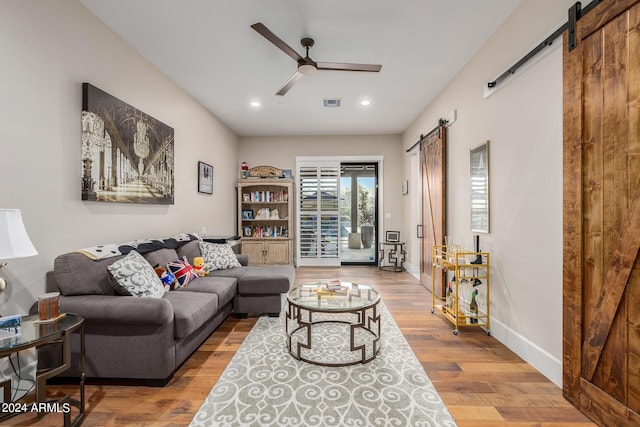 living room with a barn door, ceiling fan, and hardwood / wood-style flooring