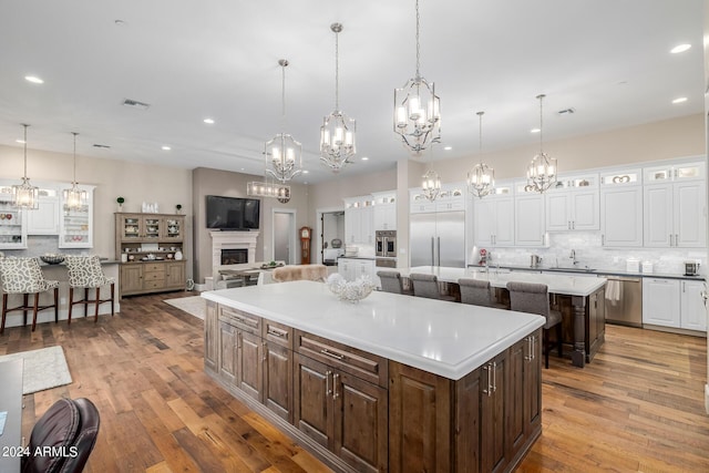 kitchen featuring stainless steel appliances, decorative light fixtures, a breakfast bar area, white cabinets, and a large island