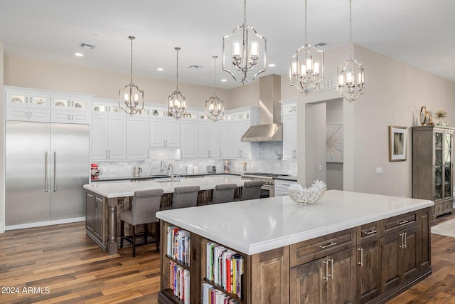 kitchen featuring wall chimney exhaust hood, white cabinetry, hanging light fixtures, and a large island with sink