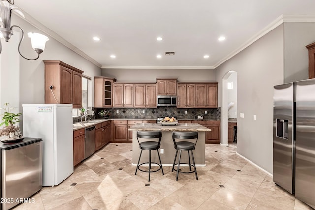 kitchen featuring a kitchen island, appliances with stainless steel finishes, backsplash, a kitchen breakfast bar, and light stone counters